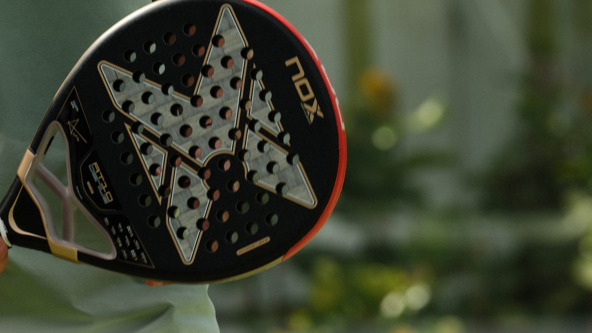 Raquette de padel en carbone posée sur un genou, au bord du court